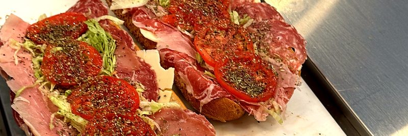 Two long rolls open on the counter, piled with sliced meats