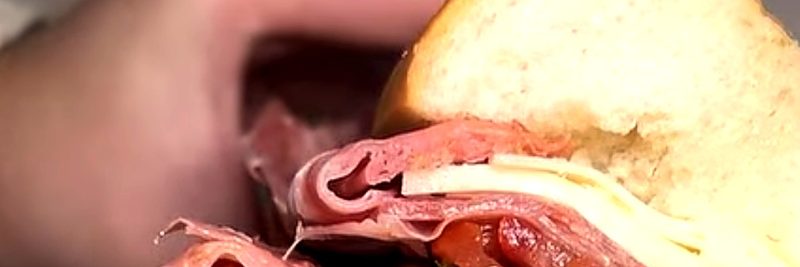 An Italian-style hoagie on a seeded roll, cut in half: sliced meats, cheese, tomato and greens